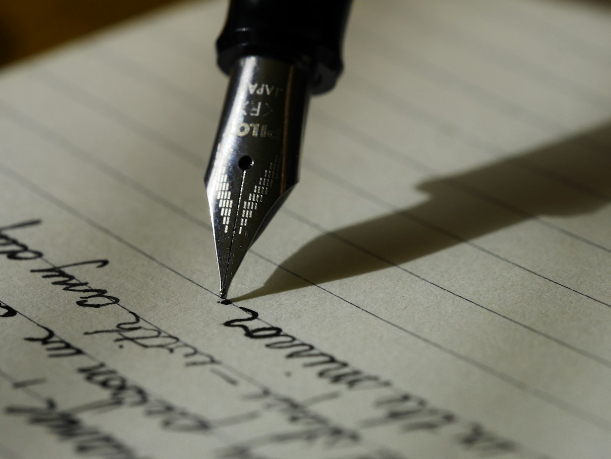 A fountain pen nib touching a ruled page